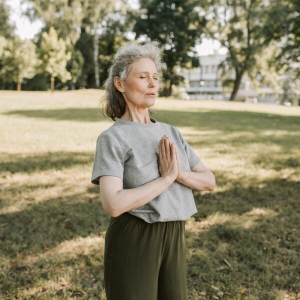 Frau führt eine Yoga-Übung auf einer Wiese im Park aus.   