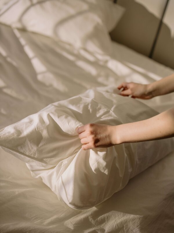 Hände beziehen vorsichtig ein weißes Kopfkissen auf einem frisch gemachten Bett.