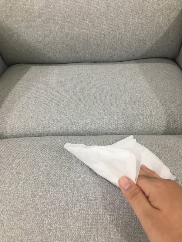 Eine Hand wischt mit einem Tuch einen Fleck von einem hellen Polstersofa.