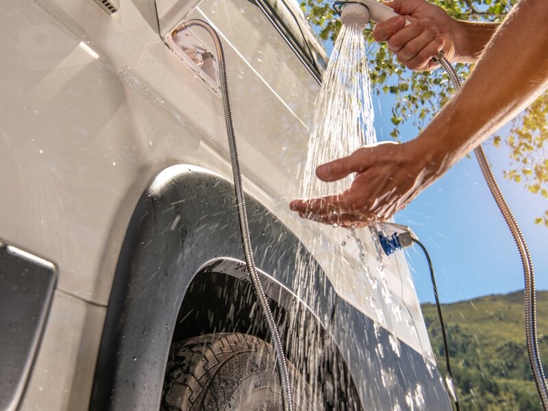 Eine Person wäscht sich bei einem Wohnmobil mit Wasser die Hände ab.