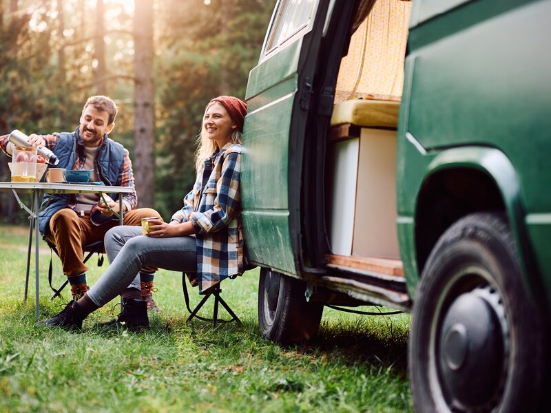 Zwei Personen sitzen entspannt vor einem grünen Camper-Van im Freien.